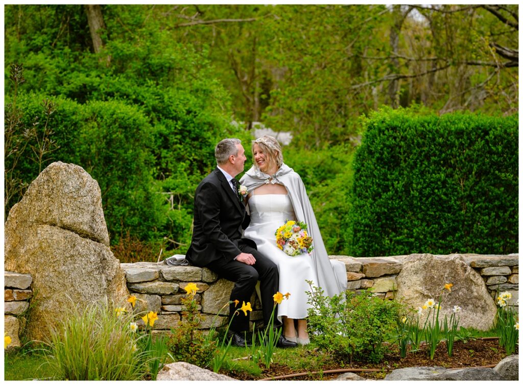 bride and groom sitting on a wall in the Sagamore Inn's gardens